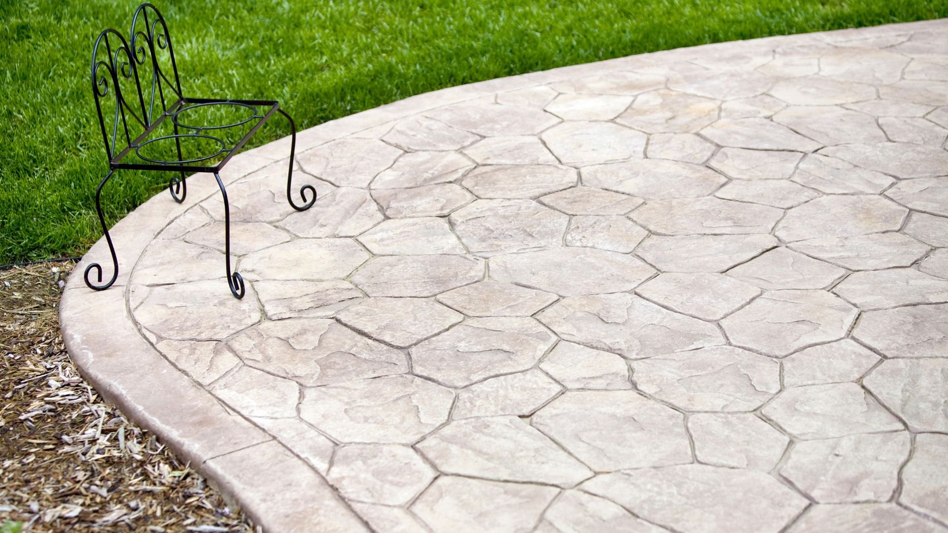 Wrought iron chair on stamped concrete patio with green grass background