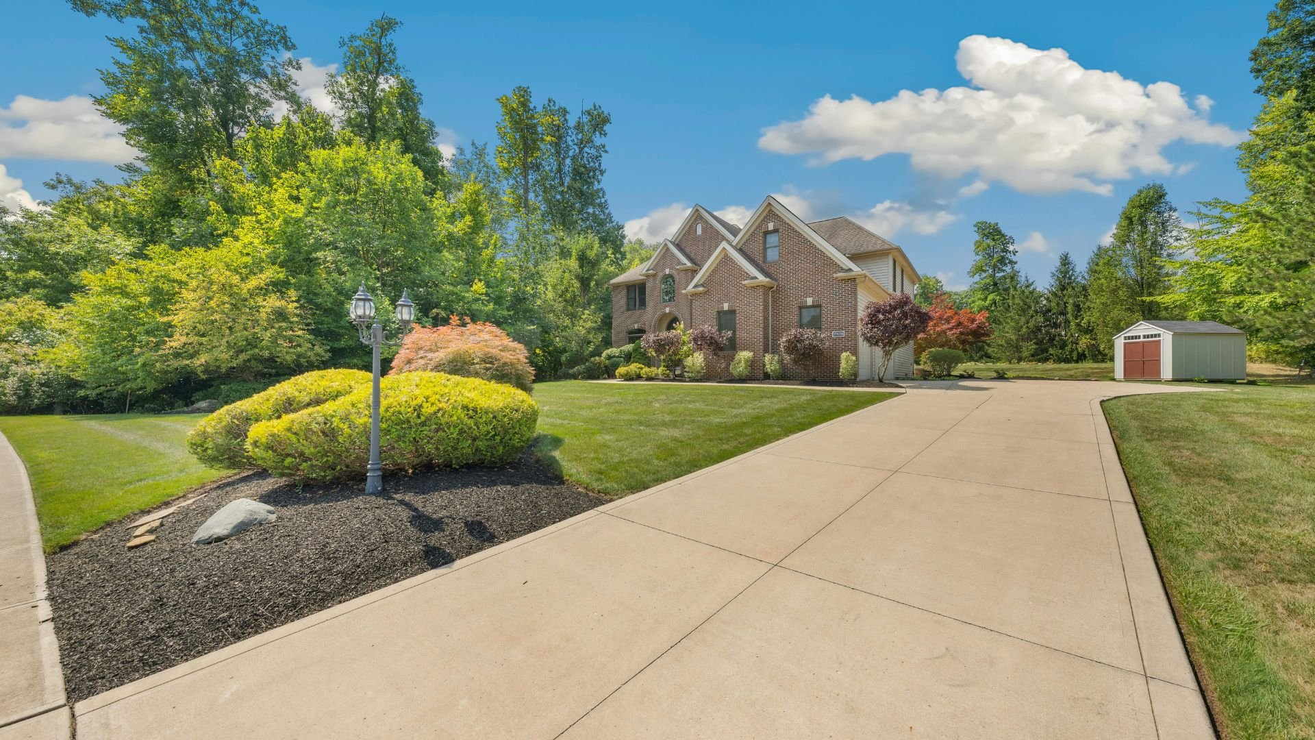 Brick house with manicured lawn, landscaped yard, and shed on sunny day