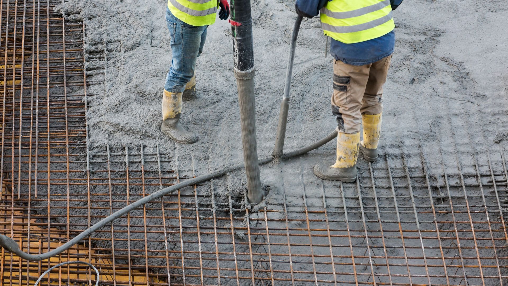 Construction workers pouring concrete on rebar mesh with vibrating tool