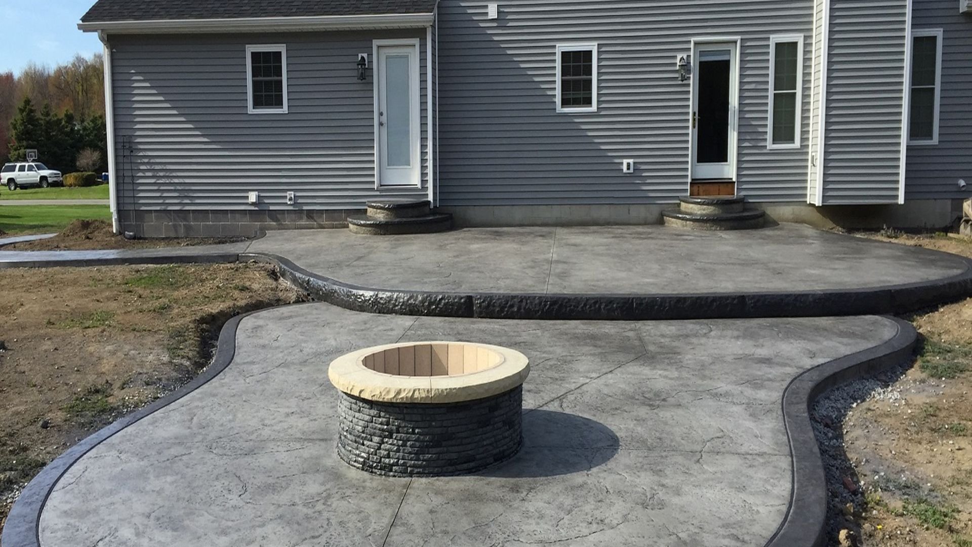 Stamped concrete patio with curved design and stone fire pit near house