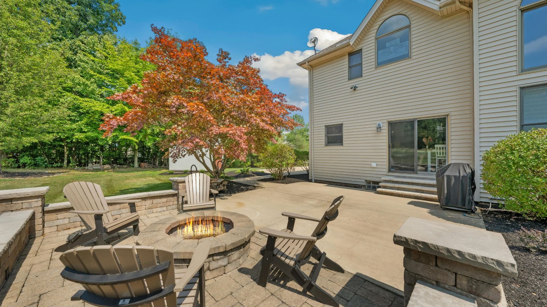 Backyard patio with fire pit, Adirondack chairs, and colorful autumn tree